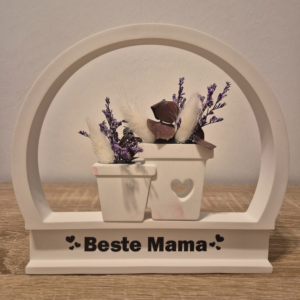 Bogen aus Gips, in der Mitte sind aus Gips zwei kleine Töpfe befestigt, die Trockenblumen enthalten und es hat die Aufschrift Beste Mama