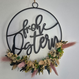 Blumenkranz mit Schriftzug frohe Ostern in der Mitte. Der untere Teil des Metallrings ist bedeckt mit Trockenblumen