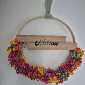 Holzring der in der Mitte einen Holzbalken mit der Aufschrift Mama hat und unterhalb mit Schleierkraut in Regenbogenfarben bestückt ist